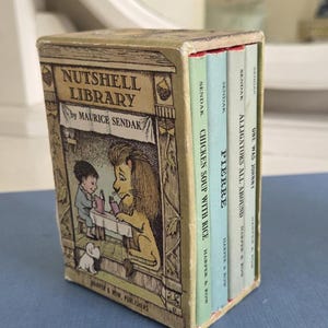 May include: A miniature boxed set of children's books titled "Nutshell Library" by Maurice Sendak. The box features an illustration of a boy and a lion reading. The set includes four small books with titles like "Chicken Soup with Rice".