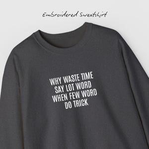 Puede incluir: Sudadera gris oscuro bordada con el texto blanco: "WHY WASTE TIME SAY LOT WORD WHEN FEW WORD DO TRICK". Las palabras están en negrita, sin serifa. El texto "Embroidered Sweatshirt" está encima.