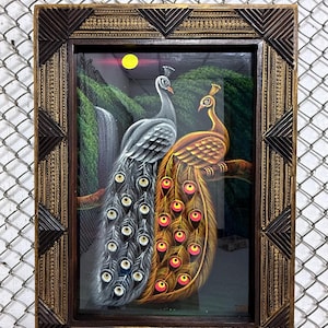 Puede incluir: Obra de arte enmarcada con dos pavos reales, uno gris y otro dorado, posados en una rama. El fondo incluye una cascada, vegetación exuberante y una luna amarilla. El marco es marrón oscuro con detalles decorativos.