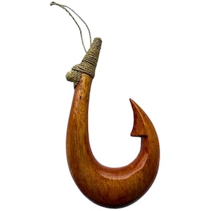 May include: A handcrafted wooden fish hook with a curved design and a pointed tip. The hook is made of polished, dark brown wood and has a wrapped section at the top with a natural fiber cord for hanging.