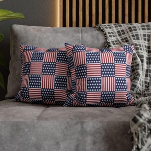 May include: Two square throw pillows featuring a repeating checkerboard pattern of red and white vertical stripes alternating with blue squares containing white stars, mimicking the design of the American flag across the entire fabric surface.