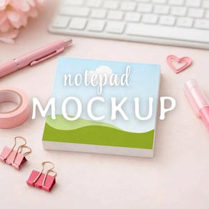 Può includere: Un mockup di blocco note con un design cielo e erba, con il testo "notepad MOCKUP". L'immagine include forniture per ufficio rosa come una penna, nastro adesivo e fermagli, insieme a una tastiera e una graffetta a forma di cuore.
