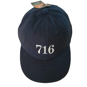 May include: A navy blue baseball cap with the number "716" embroidered in white on the front. The cap has a curved brim and a fabric-covered button on top. A tag is attached to the cap.