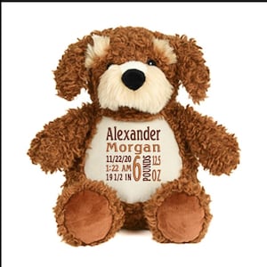 May include: A brown plush dog with a cream-colored muzzle and inner ears. The dog has a white belly with the embroidered text "Alexander Morgan" and birth details: 6 pounds, 12.5 ounces, 19 1/2 inches, and the date and time of birth.