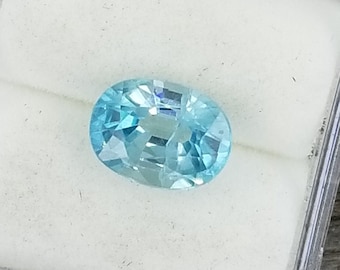 Könnte beinhalten: Ein ovaler, hellblauer Edelstein in einer durchsichtigen Plastikbox. Der Edelstein ist facettiert und hat einen leichten Schimmer.