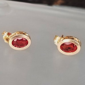Puede incluir: Un par de pendientes de oro con piedras preciosas ovaladas rojas.