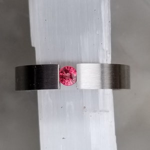 May include: A silver ring with a single, round, pink gemstone set in the center.