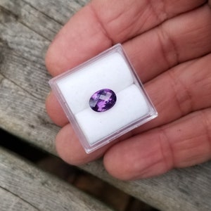 May include: A purple oval gemstone in a small white box