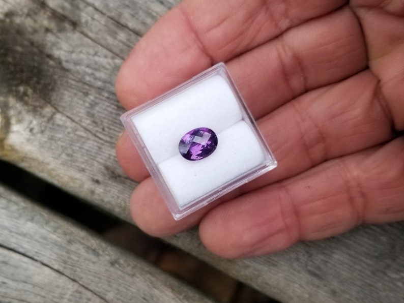 May include: A purple oval gemstone in a small white box