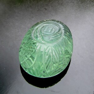 Pode incluir: Um peso de papel de vidro verde com um design floral esculpido. O peso de papel tem formato oval e uma superf&iacute;cie lisa e polida.