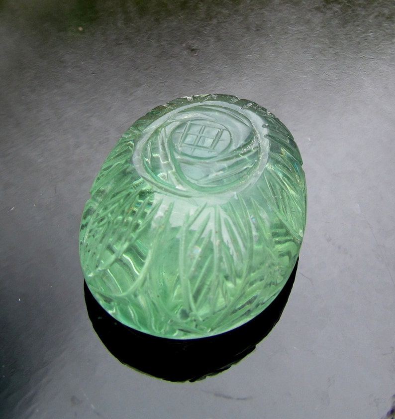 Pode incluir: Um peso de papel de vidro verde com um design floral esculpido. O peso de papel tem formato oval e uma superf&iacute;cie lisa e polida.