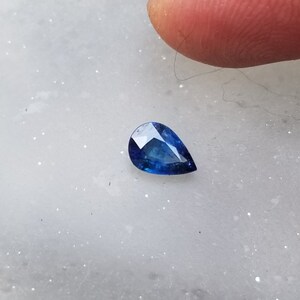 Puede incluir: Una piedra preciosa azul en forma de pera sobre una superficie blanca.
