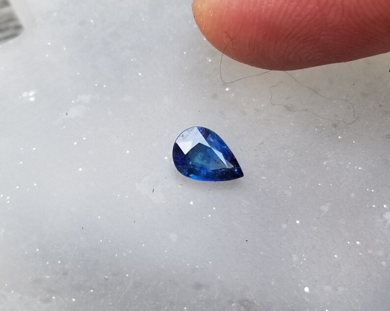 Puede incluir: Una piedra preciosa azul en forma de pera sobre una superficie blanca.