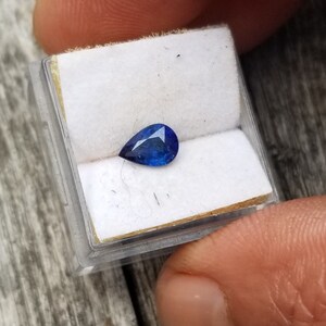 Puede incluir: Una piedra preciosa azul en forma de l&aacute;grima en una peque&ntilde;a caja blanca.