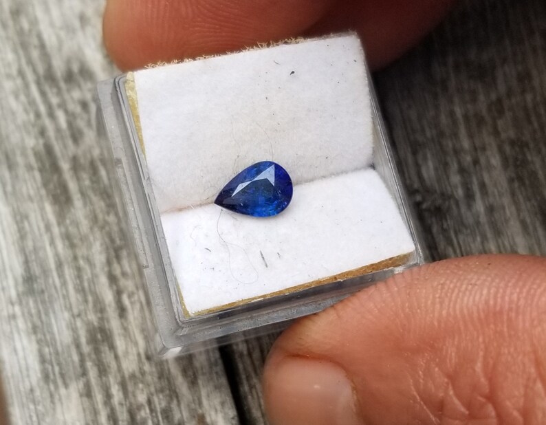 Puede incluir: Una piedra preciosa azul en forma de l&aacute;grima en una peque&ntilde;a caja blanca.