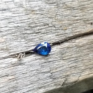 Puede incluir: Una piedra preciosa azul en forma de l&aacute;grima sobre una superficie de madera desgastada.