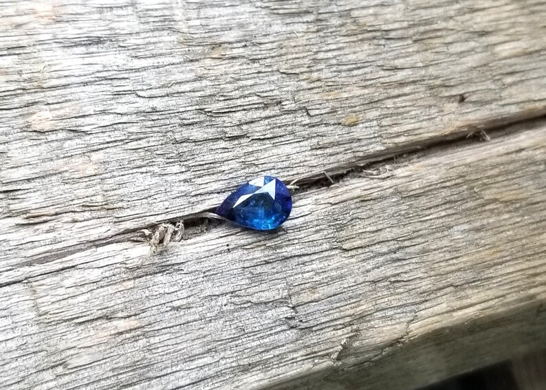 Puede incluir: Una piedra preciosa azul en forma de l&aacute;grima sobre una superficie de madera desgastada.