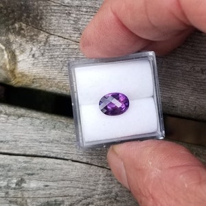 May include: A purple oval gemstone in a small white box.