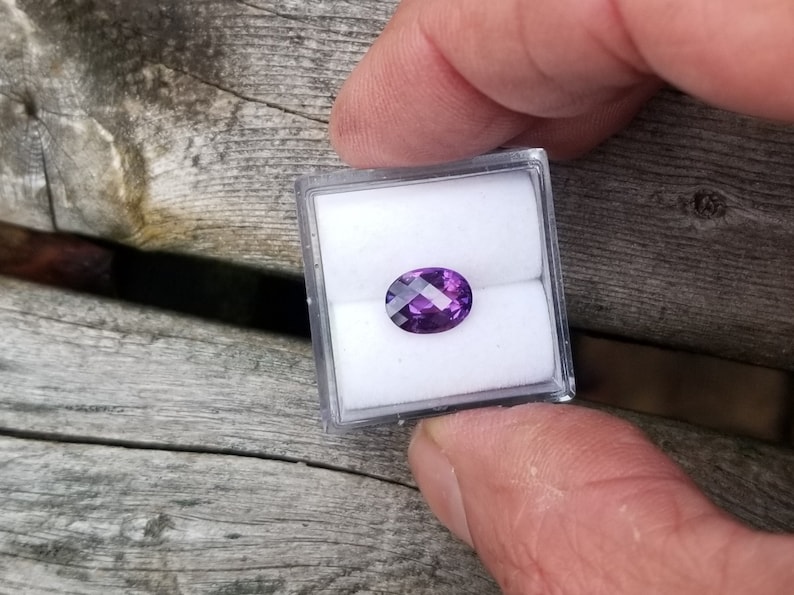 May include: A purple oval gemstone in a small white box.