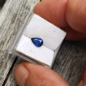 Puede incluir: Una piedra preciosa de zafiro azul en forma de l&aacute;grima en una peque&ntilde;a caja blanca.