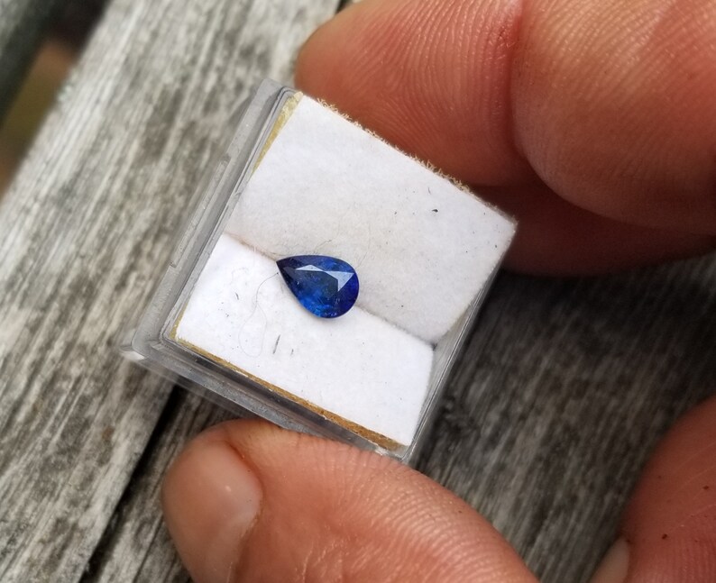 Puede incluir: Una piedra preciosa de zafiro azul en forma de l&aacute;grima en una peque&ntilde;a caja blanca.