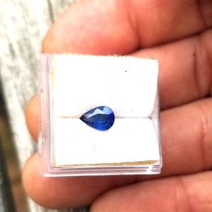 Puede incluir: Una piedra preciosa de zafiro azul en forma de pera en una peque&ntilde;a caja blanca.