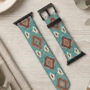 Op de afbeelding: Twee turquoise horlogebandjes met een geometrisch patroon in tinten roest, wit en bruin. De bandjes hebben zwarte hardware en worden gepresenteerd op een licht houten oppervlak. Horloge-accessoire.