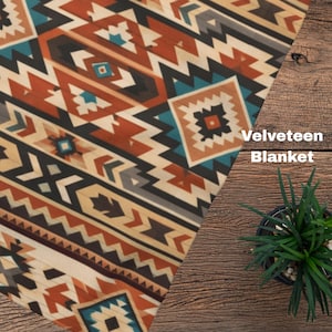 May include: A velveteen blanket featuring a geometric pattern in shades of burnt orange, teal, cream, black, and brown. The fabric displays repeating diamond and chevron shapes arranged in diagonal stripes across the surface of the textile.
