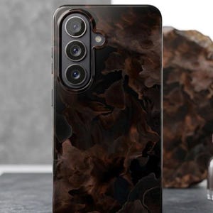 Puede incluir: Funda de teléfono inteligente con un diseño marrón oscuro y arremolinado. La funda tiene un acabado brillante y un módulo de cámara con tres lentes. El fondo es una superficie gris neutra.