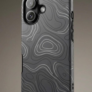 May include: A dark gray phone case with a topographic map design. The case features a series of white and gray contour lines, creating a layered effect. The case has a camera cutout with two lenses and a flash, and buttons on the side.