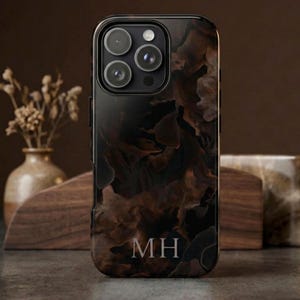 Puede incluir: Funda de teléfono inteligente negra con un diseño abstracto en espiral marrón y beige. La funda tiene un recorte para la cámara y las iniciales "MH" en la parte inferior. La funda se muestra sobre una superficie de madera.