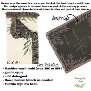May include: A woven blanket featuring a cream-colored front with green olive branch illustrations and a dark-colored backside where the design appears in reversed tones. The blanket has fringed edges and includes care instructions for machine washing.