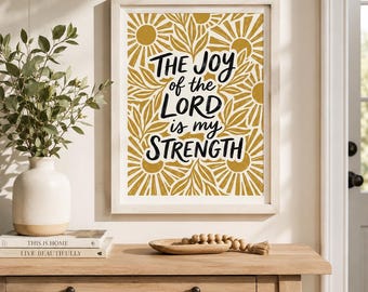 May include: A framed wall art print featuring the black text THE JOY of the LORD is my STRENGTH centered over a mustard yellow and white pattern of stylized suns and leaves. The print is displayed in a light-colored wooden frame.