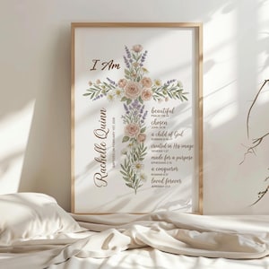 Puede incluir: Un estampado enmarcado con un dise&ntilde;o de cruz floral. La cruz est&aacute; adornada con rosas rosas, lavanda y vegetaci&oacute;n. El texto incluye "I Am", "Rachelle Quinn" y vers&iacute;culos b&iacute;blicos como "beautiful" y "chosen". El marco es de color marr&oacute;n claro.