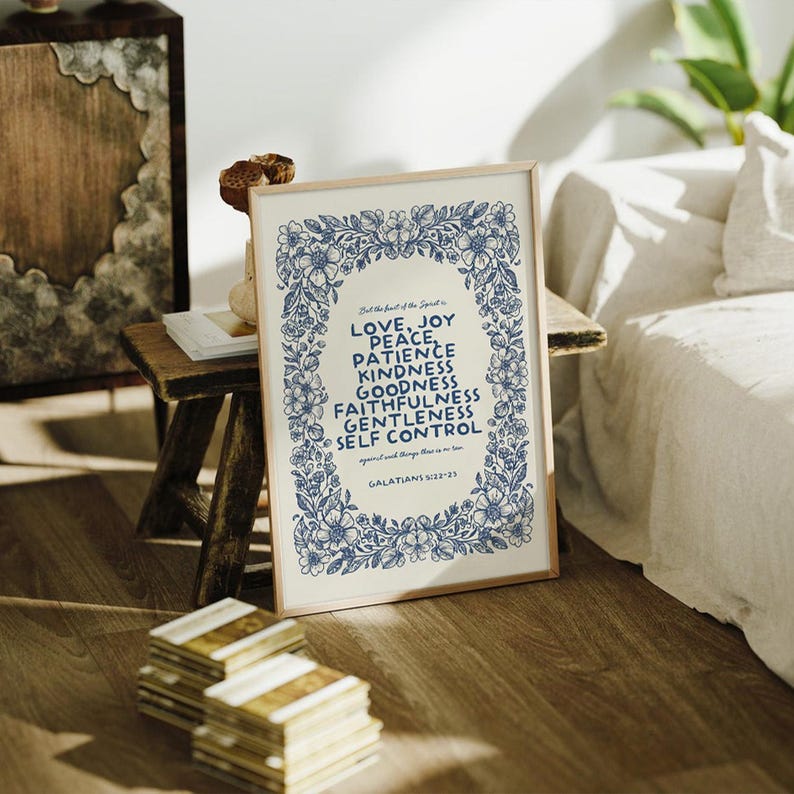 May include: A framed print with a floral border in blue and white. The text reads "LOVE, JOY, PEACE, PATIENCE, KINDNESS, GOODNESS, FAITHFULNESS, GENTLENESS, SELF CONTROL" from Galatians 5:22-23. The print is displayed on a wooden floor.
