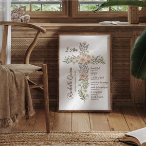 Puede incluir: Un estampado enmarcado con un dise&ntilde;o de cruz floral y las palabras "I Am". La cruz est&aacute; adornada con flores y vegetaci&oacute;n de colores pastel. El nombre "Rachelle Quinn" est&aacute; escrito verticalmente a la izquierda. El estampado incluye texto inspirador.