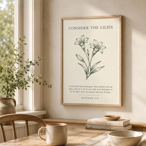 May include: A framed wall art print on a cream background featuring a black line drawing of lilies. The text reads: CONSIDER THE LILIES of the field, how they grow: they neither toil nor spin; and yet I say to you that even Solomon in all his glory was not arrayed like one of these. MATTHEW 6:28.