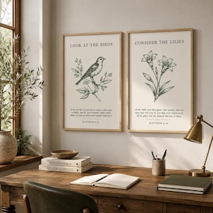 May include: Two rectangular wall art prints in light wood frames featuring botanical illustrations. The left print shows a bird on a branch with the text LOOK AT THE BIRDS and Matthew 6:26. The right print shows lilies with CONSIDER THE LILIES and Matthew 6:28.