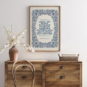 May include: A framed print with a cream background and blue floral border. The text reads "LOVE, JOY, PEACE, PATIENCE, KINDNESS, GOODNESS, FAITHFULNESS, GENTLENESS, SELF CONTROL" with the scripture reference Galatians 5:22-23. The print is displayed on a wooden dresser.