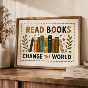 May include: A framed rectangular print featuring the text READ BOOKS CHANGE THE WORLD in bold, colorful letters. The design includes a row of eight illustrated books with decorative spines, flanked by leafy branches and small heart icons.
