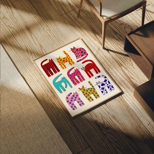 May include: A framed art print featuring a repeating pattern of stylized cats in various colors and patterns. The cats are depicted in red, yellow, pink, blue, and purple, with designs including stripes, polka dots, and stars. The print is displayed on a light-colored wooden floor.