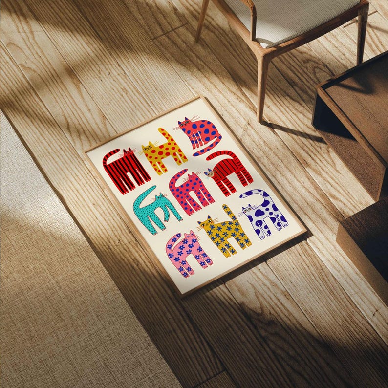 May include: A framed art print featuring a repeating pattern of stylized cats in various colors and patterns. The cats are depicted in red, yellow, pink, blue, and purple, with designs including stripes, polka dots, and stars. The print is displayed on a light-colored wooden floor.