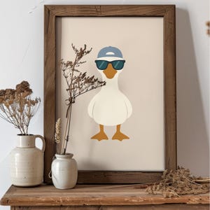 Pu&ograve; includere: Una stampa artistica incorniciata con un'oca dei cartoni animati con occhiali da sole e un berretto da baseball blu. L'oca ha un corpo bianco, un becco e zampe arancioni, su uno sfondo neutro. La cornice &egrave; in legno.