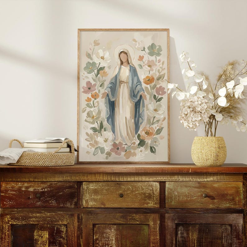 May include: A framed print of a religious figure surrounded by flowers. The figure is depicted in a long white dress and blue shawl, with a halo. The floral arrangement includes pastel colors like pink, orange, and green. The artwork is displayed on a wooden cabinet.