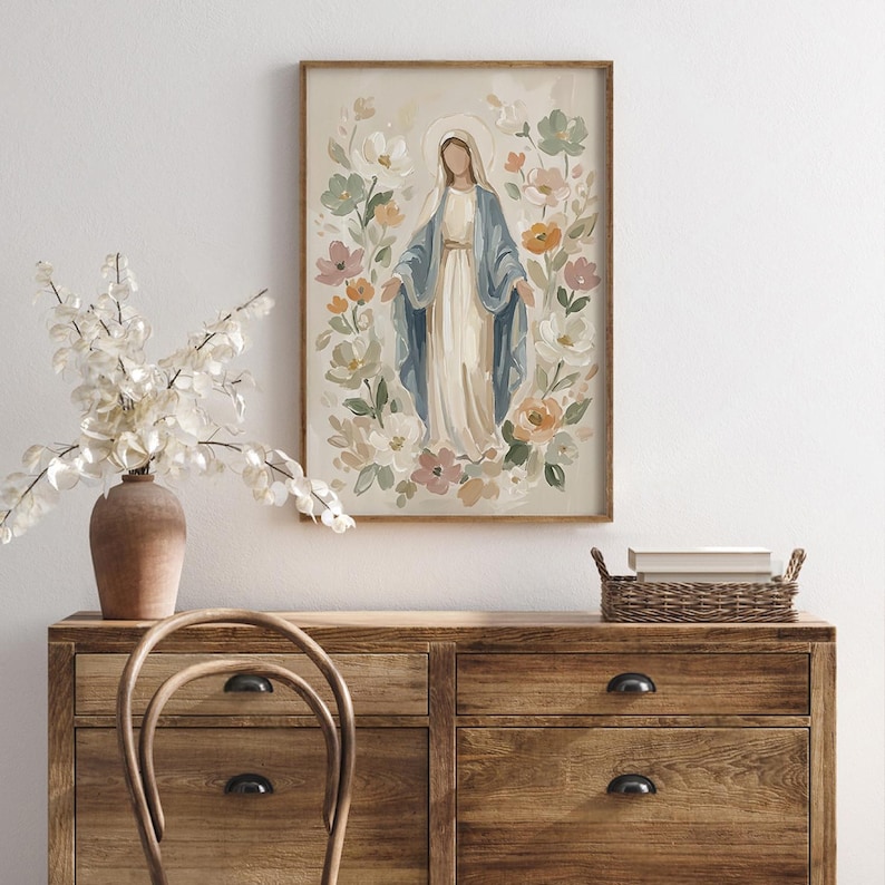 May include: A framed print of a religious figure surrounded by flowers. The figure is depicted in a long white dress and blue shawl, with a halo. The artwork has a soft, pastel color palette and is displayed on a wooden dresser.
