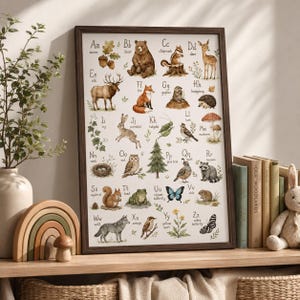 May include: A framed educational alphabet poster featuring watercolor illustrations of woodland animals and nature elements, with each letter from A to Z paired with a corresponding creature or plant, including an acorn, bear, and zebra butterfly.