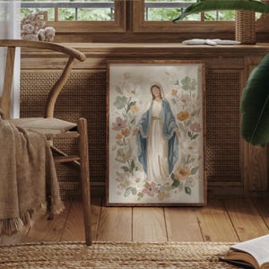 May include: A framed watercolor print of a religious figure surrounded by flowers. The figure is depicted in a white dress and blue shawl, with a halo. The floral arrangement includes pink, yellow, and green blooms. The frame is a warm brown color.