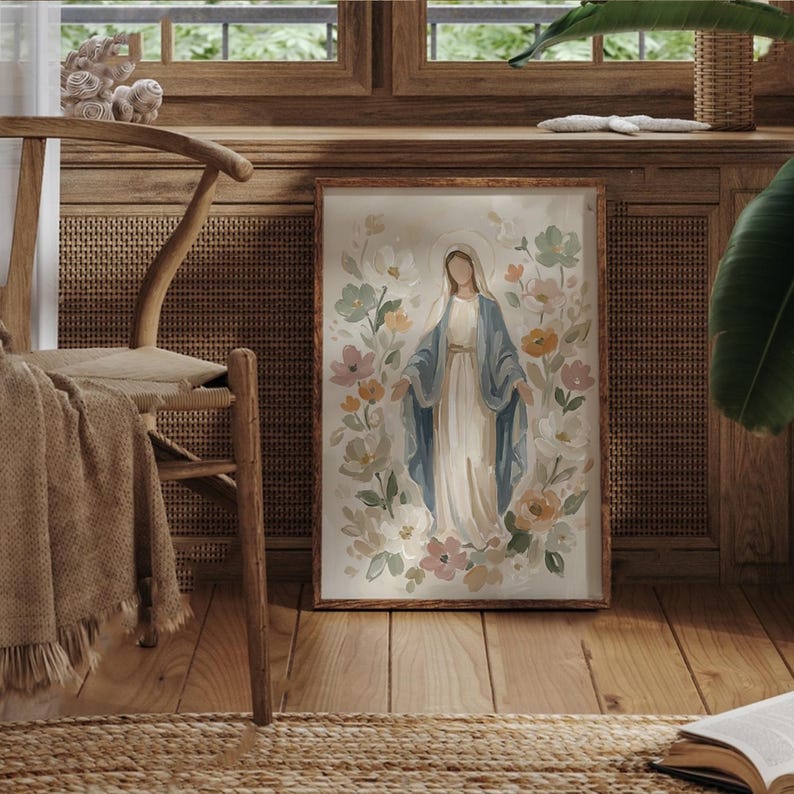 May include: A framed watercolor print of a religious figure surrounded by flowers. The figure is depicted in a white dress and blue shawl, with a halo. The floral arrangement includes pink, yellow, and green blooms. The frame is a warm brown color.