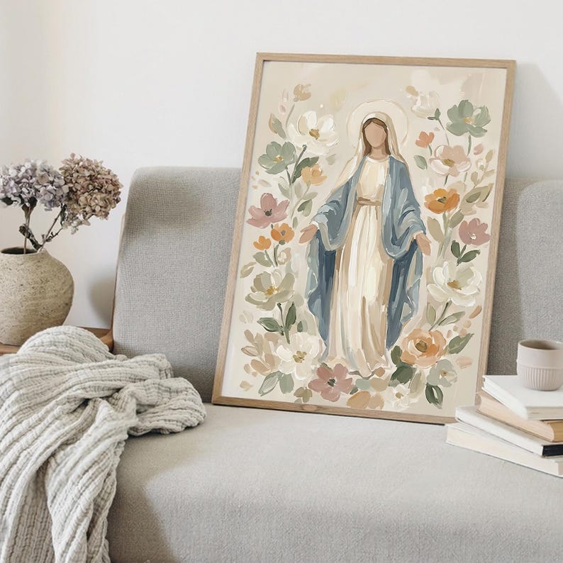 May include: A framed art print featuring a religious figure surrounded by flowers. The figure is depicted in a white dress and blue shawl, with a halo. The floral arrangement includes white, pink, and orange blooms. The artwork is set against a neutral background.