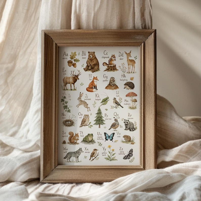 May include: A framed alphabet wall art print featuring watercolor illustrations of animals and nature elements for each letter from A to Z, including a bear, fox, owl, and wolf, set within a simple light brown wooden frame with a white background.